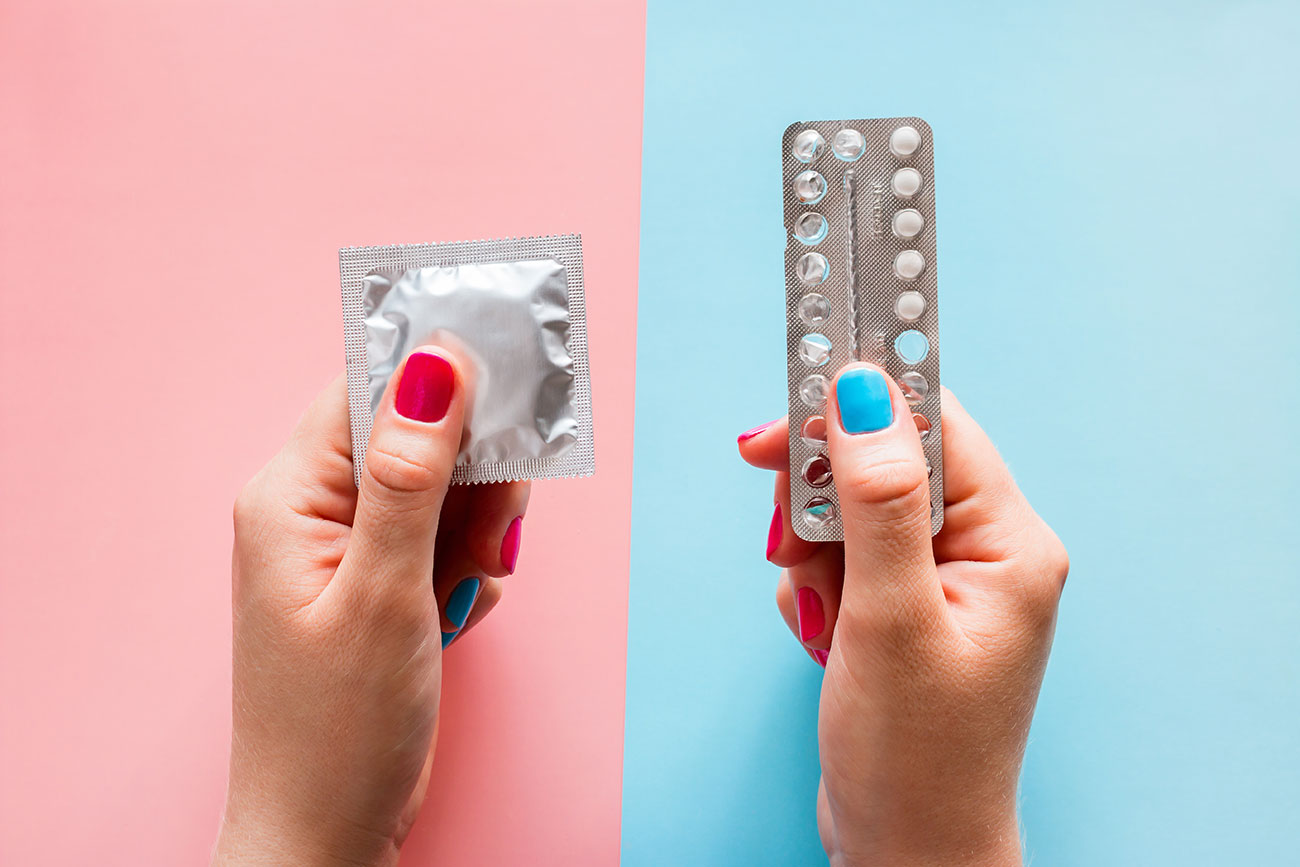 Kondom in der linken Hand und Antibabypille in der rechten Hand